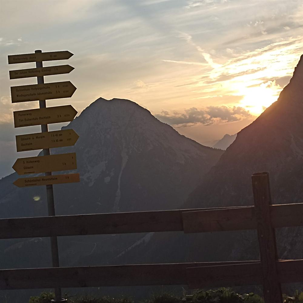 Wegweiser vor Bergen im Sonnenuntergang
