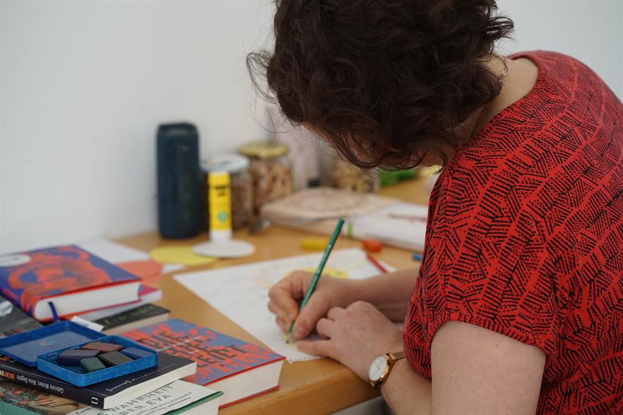Veronika schreibt an einem Tisch voller Bücher